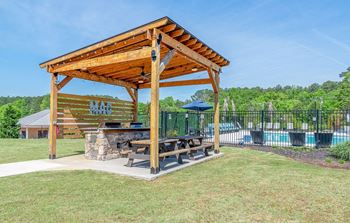 A picnic table under a wooden pavilion next to a swimming pool